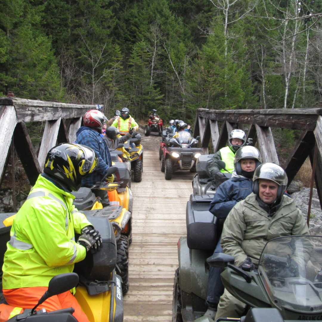 A group of people on atvs riding across a bridge.